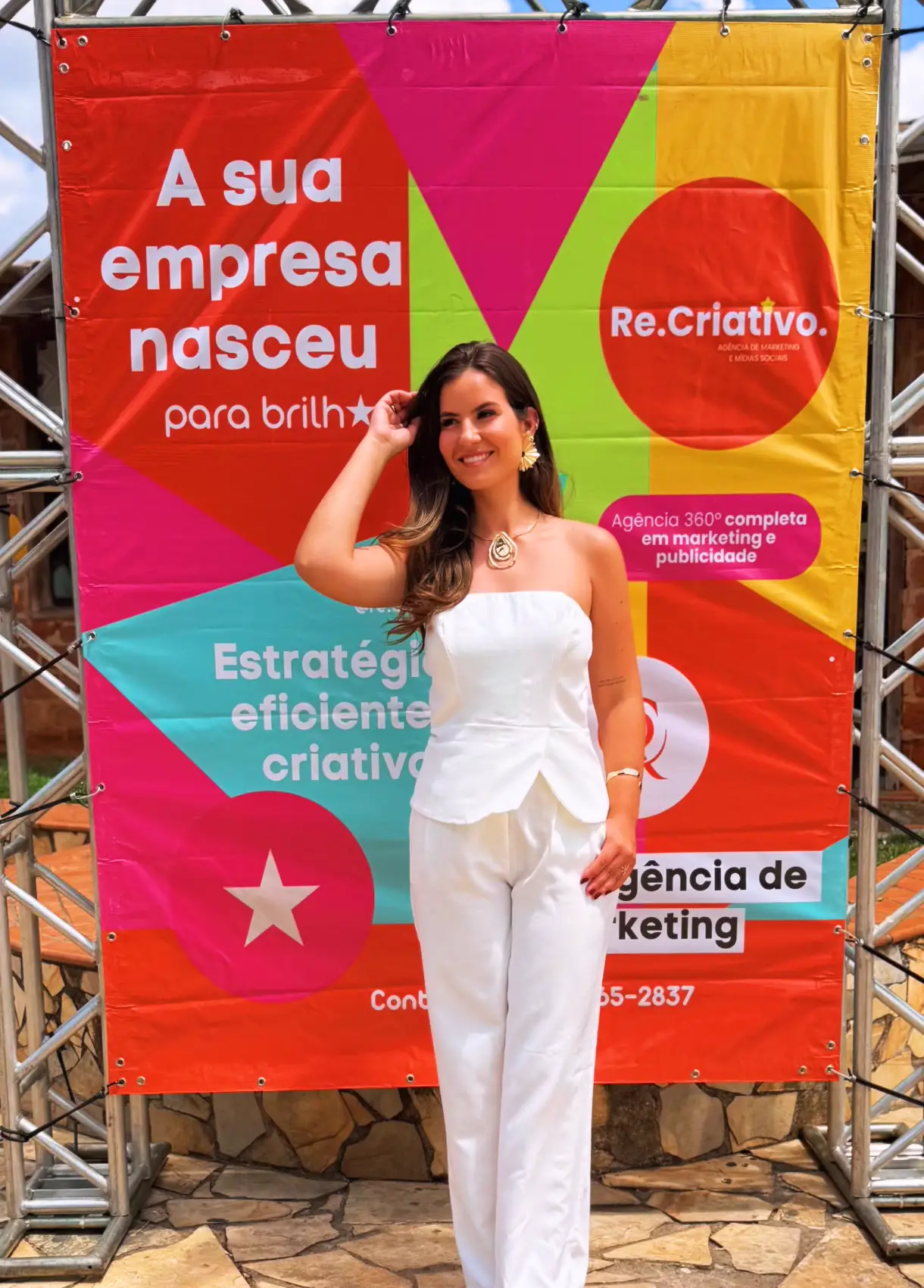 Izabelle Rezende diante do banner da Re.Criativo com a frase “A sua empresa nasceu para brilhar.”